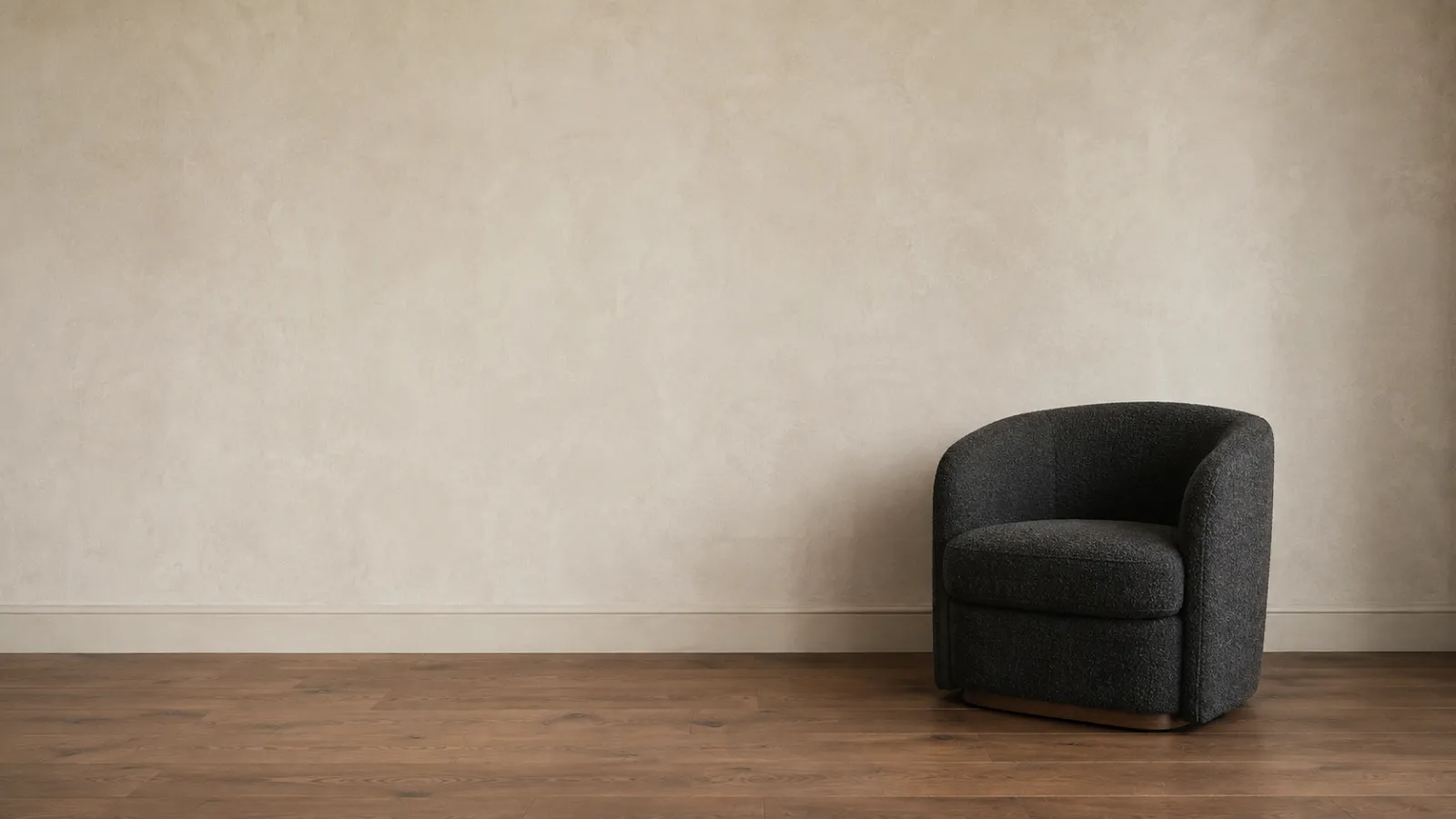 A single charcoal bouclé armchair against a wide bare wall, an example of visual rest in home decor.