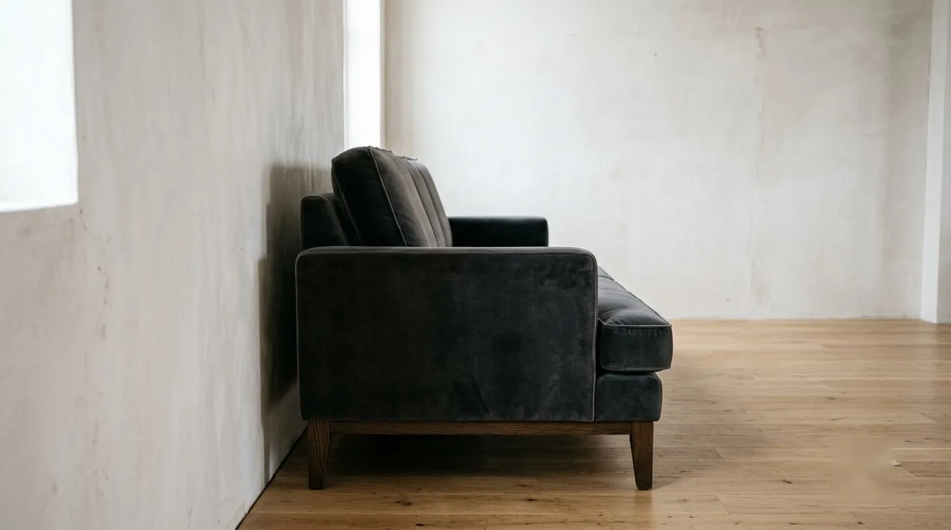 A charcoal velvet sofa pulled a few inches off the wall creates a soft shadow line in a calm living room.