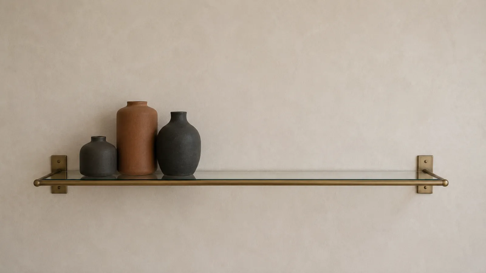 Charcoal and terracotta stoneware vases grouped tightly on a brass shelf, leaving a deliberate gap.