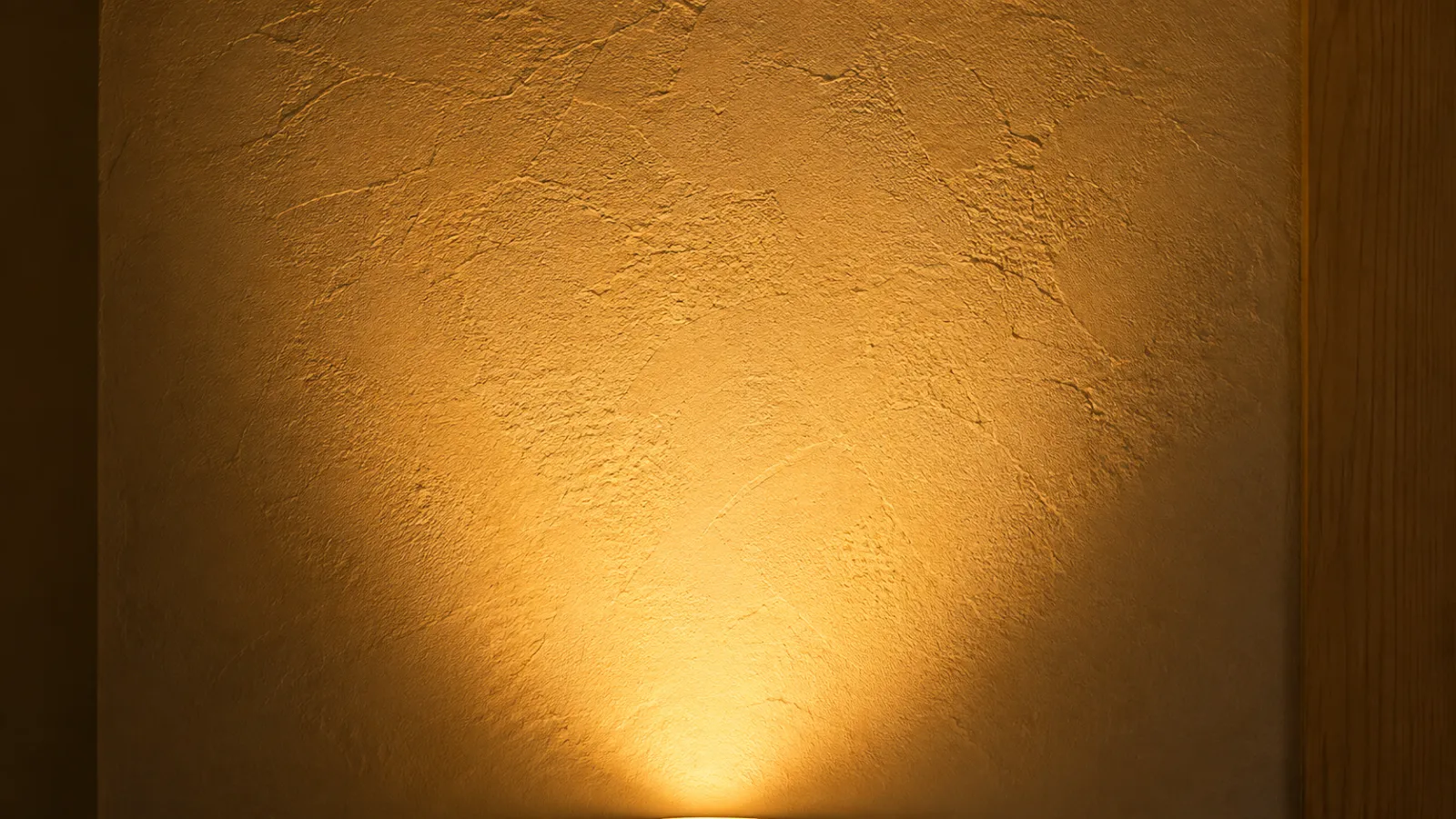 Lamplight bouncing off a cream wall and oak console, warming the whole corner.